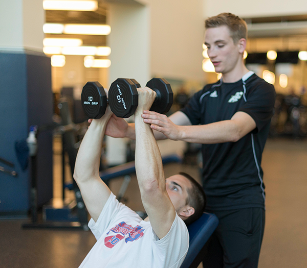 A personal trainer working with someone using dumbbells